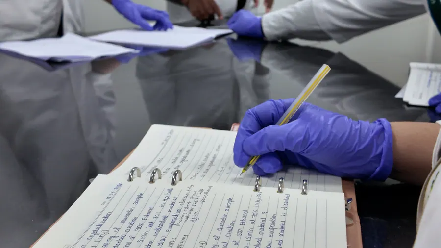 A gloved hand writing in a lab notebook
